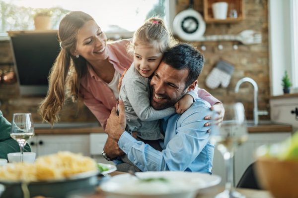 Young happy parents embracing with their small daughter during lunch at dining table.
